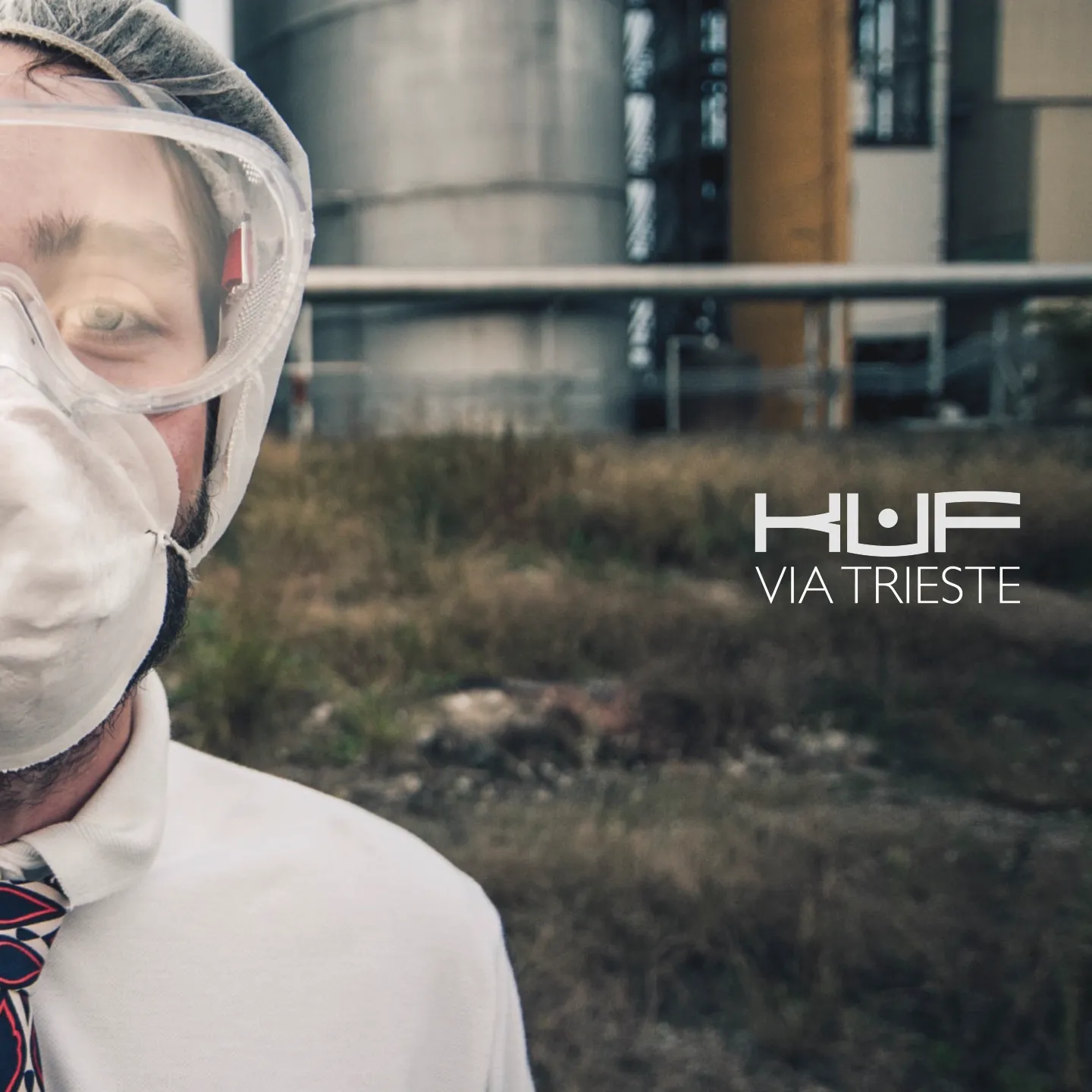 Copertina di Via Trieste, un ragazzo con mascherina e occhiali protettivi davanti a dei silos industriali, con la scritta KUF Via Trieste
